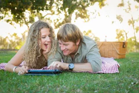 Playful Loving Couple Using a Touch Pad Computer at Their Picnic Outside. Stock Photos