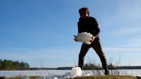 Playful man breaks a block of ice near frozen river on nature in sunny day. Stock Footage 311860016