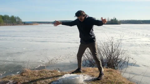 Playful man breaks a block of ice near frozen river on nature in sunny day. Stock Footage 311865902