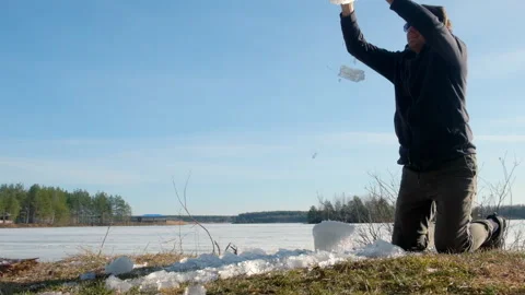 Playful man breaks a block of ice near frozen river on nature in sunny day. Stock Footage 311866284
