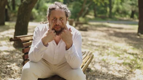 Playful man making funny faces on a park bench Vídeos de archivo 323300105