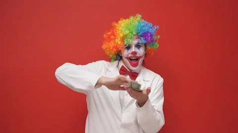 A playful, positive, funny clown throws money, dollars out of his hands on an Stock Footage 157639249