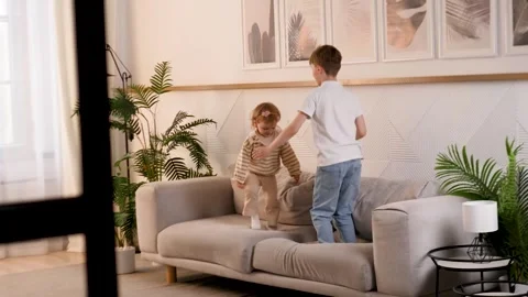Playful siblings enjoy spending time together at home jumping on the couch in a Stock Footage 312158656