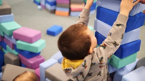 Playful toddlers constructing towering foam block structures, enhancing fine Stock Footage 303820803