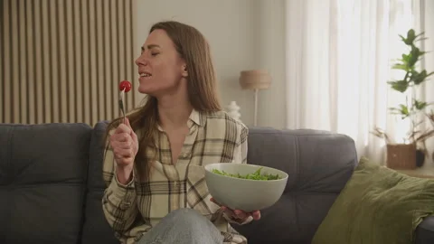 Playful Woman Singing Into Fork While Eating Salad, Enjoying Fun Moment At Home Stock Footage 303087323