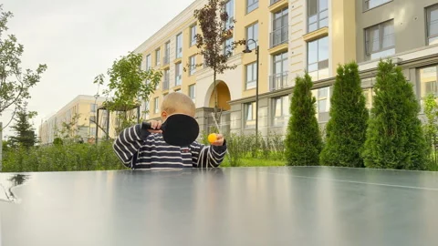 A playful young boy covers his face with a black ping pong paddle Stock Footage 344972014