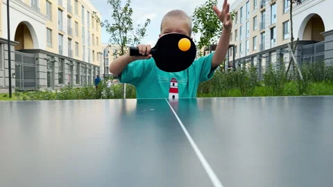 A playful young boy hides his face behind a black ping pong paddle. Stock Footage 344969041