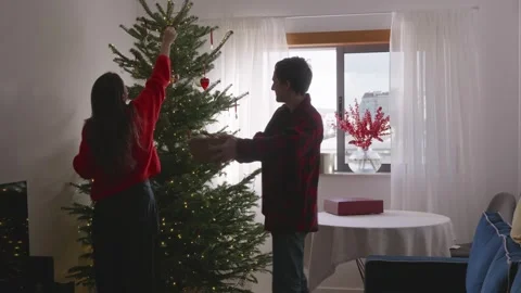 Playful young couple dancing, decorating Christmas tree in cozy living room Stock Footage 324923681