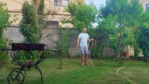Playful young man in the backyard watering grass during a picnic and dancing Stock Footage