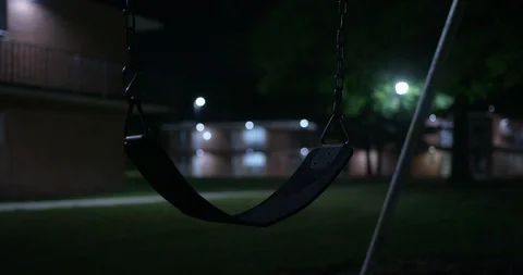 Playground swing gently swinging at night in an empty apartment complex. Stock Footage