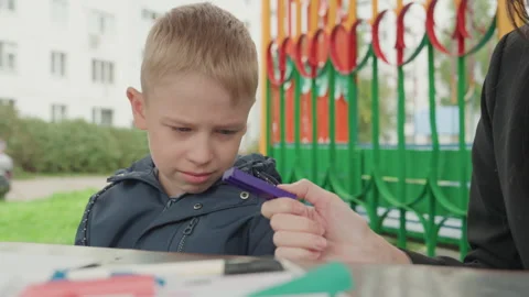Playground table child head down parent offers marker and comfort prepare school Stock Footage 333096529