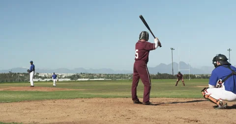 Playing baseball, batter in maroon uniform preparing to hit pitched ball Stock Footage 297343565