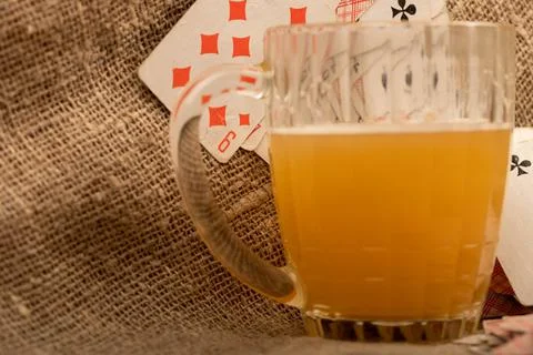 Playing cards and a mug of light unfiltered beer on a table covered with coar Stock Photos