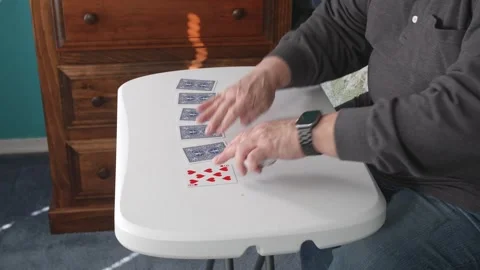 Playing Cards at a Table, a Man Creates Sequences and Moves Cards in a Room Stock Footage 335653143