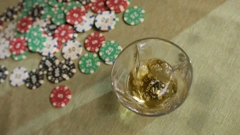 A playing chip falls into a glass of whiskey on a poker table Stock Footage 225884234