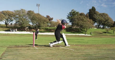 Playing cricket, female batter hitting ball on field during match Stock Footage 297438987