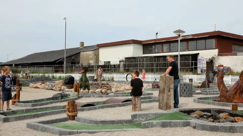 Playing a game of minigolf on a course with figures of dinosaurs Stock Footage 40687065