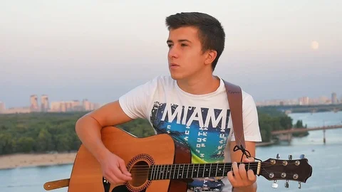 Playing guitar on sunset and river background Stock Footage 107940763