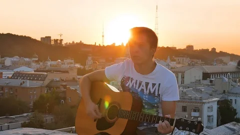 Playing guitar on sunset with light leaks and city horizon Stock Footage 107940732