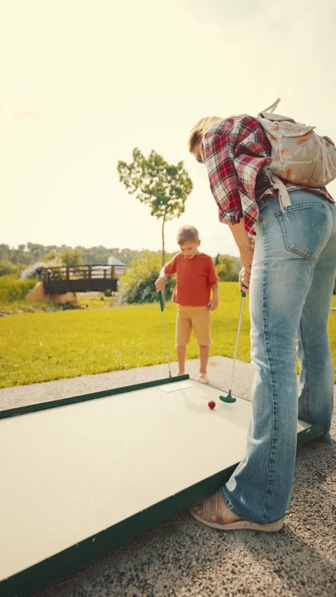 Playing mini golf in the park on a sunny day with a child and adult enjoying Stock Footage 339462083