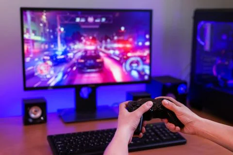 Playing racing games on computer concept. Hand holds the joystick. In the bac Stock Photos