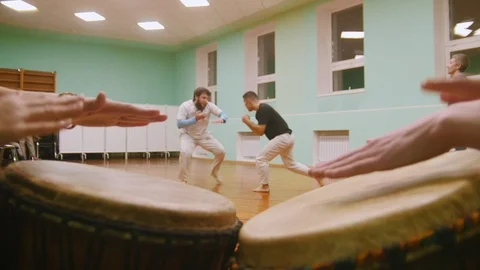 Playing a two musical instruments atabaque on background male fighter performs Stock Footage 99040987