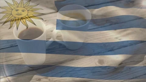 Playing Uruguay flag overlay rippling over wood table, mugs reflecting blue Stock Footage 332404752