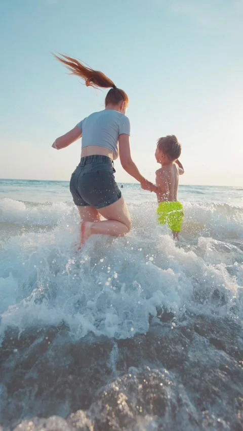 Playing in the waves at the beach on a sunny day with a child running in the Stock Footage 338301421