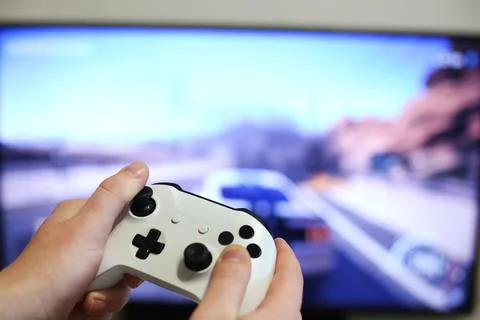 Plays racing games on TV while holding white gamepad Stock Photos