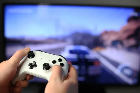 Plays racing games on TV while holding white gamepad Stock Photos