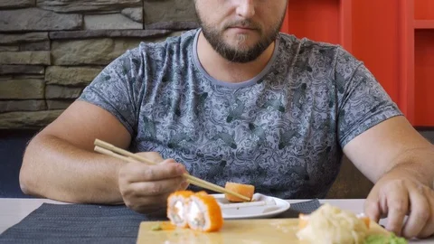 Pleasant chubby man with a beard in a sushi bar, funny eating rolls. Does not Video stock 115335767