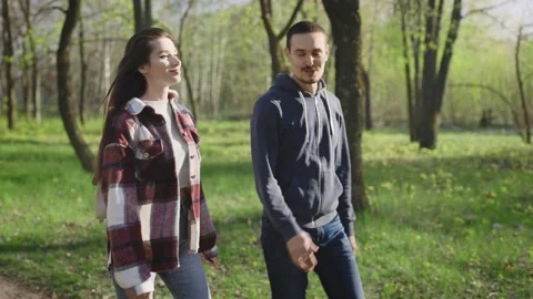 A pleasant couple of young people in casual clothes are walking in the park in Stock Footage 201838341