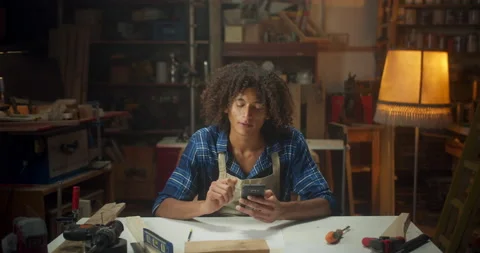 Pleasant curly young carpenter man using mobile device online get inspiration in Stock Footage 140615824