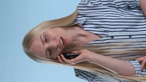 Pleasant-looking young lady speaking with somebody by smartphone on blue Stock Footage 130180985