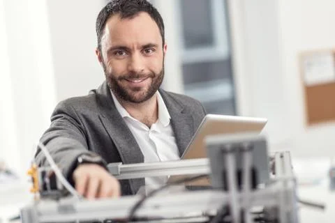 Pleasant man posing while solving problems with 3D printer Stock Photos