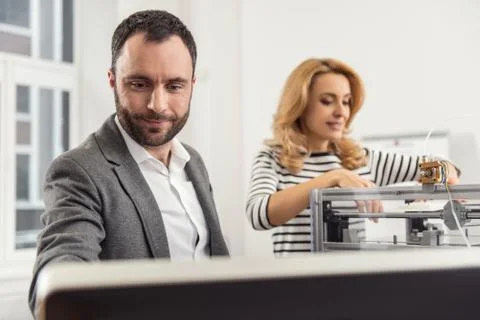 Pleasant man reading from computer while woman launching 3D printer Stock Photos