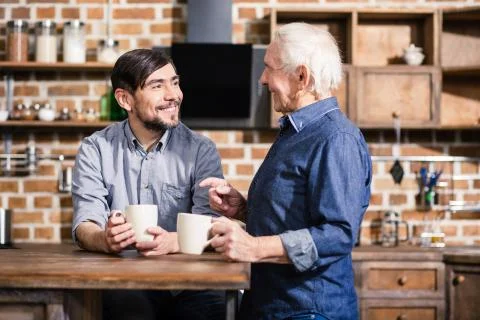 Pleasant smiling man drinking tea with his son Stock Photos