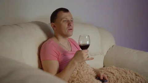 Pleasant young man drinking wine watching tv in the evening while sitting on Stock Footage 139355670