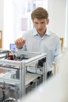 Pleasant young man looking for error in 3D printer mechanism Stock Photos