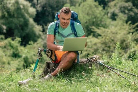 Pleasant young man with prosthesis using his laptop in the forest Stock Photos
