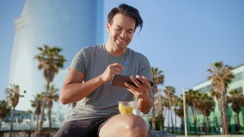 Pleasant young man using smart device to watch YouTube video eating pineapple Stock Footage 109419213