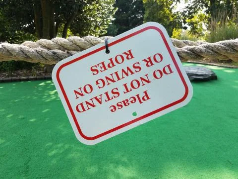 Please do not stand or swing on rope sign upside down on miniature golf course Stock Photos