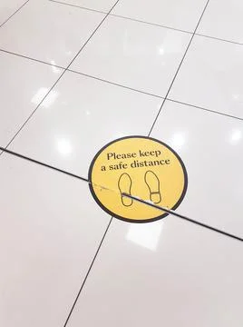 Please keep a safe distance yellow floor sticker on a tiled floor Stock Photos