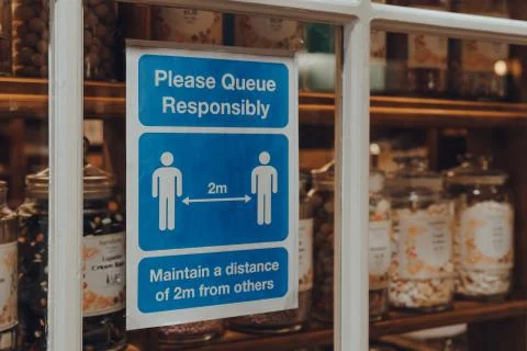 Please Queue Responsibly social distancing sign a window of a shop in Broadwa Stock Photos