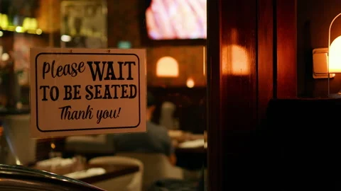 PLEASE WAIT TO BE SEATED sign at an entrance of a busy restaurant Stock Footage 207558339