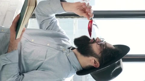 Pleased bearded man drinking red wine while reading a book at home. Stock Footage 152980292