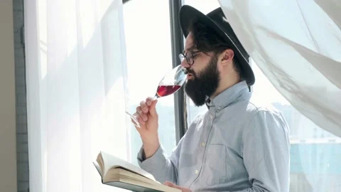 Pleased bearded man drinking red wine while reading a book at home. Stock Footage 154206047