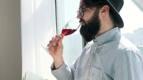 Pleased bearded man drinking red wine while reading a book at home. Stock Footage 155404828