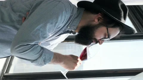 Pleased bearded man drinking red wine and admiring view form window at home. Stock Footage 155641862