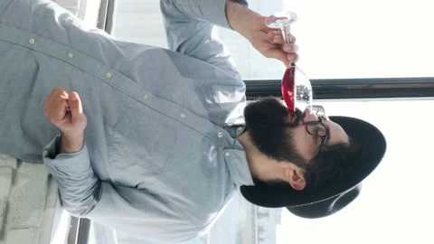 Pleased bearded man drinking red wine and admiring view form window at home. Stock Footage 155760523